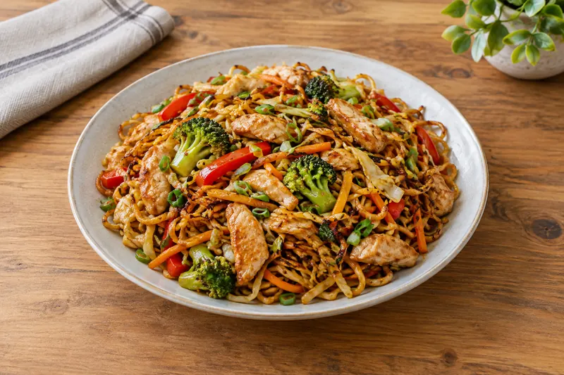 Chicken chow mein in a wok with beansprouts, spring onion and glossy noodles
