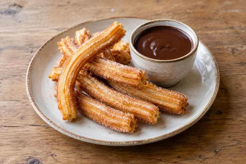 A plate of sugared ridged churros beside a small cup of thick dark drinking chocolate