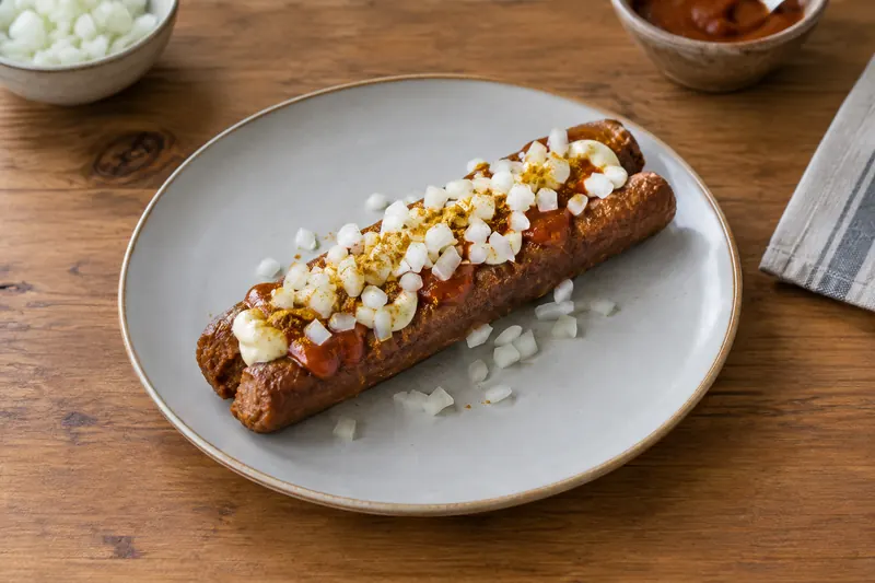Split fried frikandel sausages topped with mayonnaise, curry ketchup and chopped raw onion