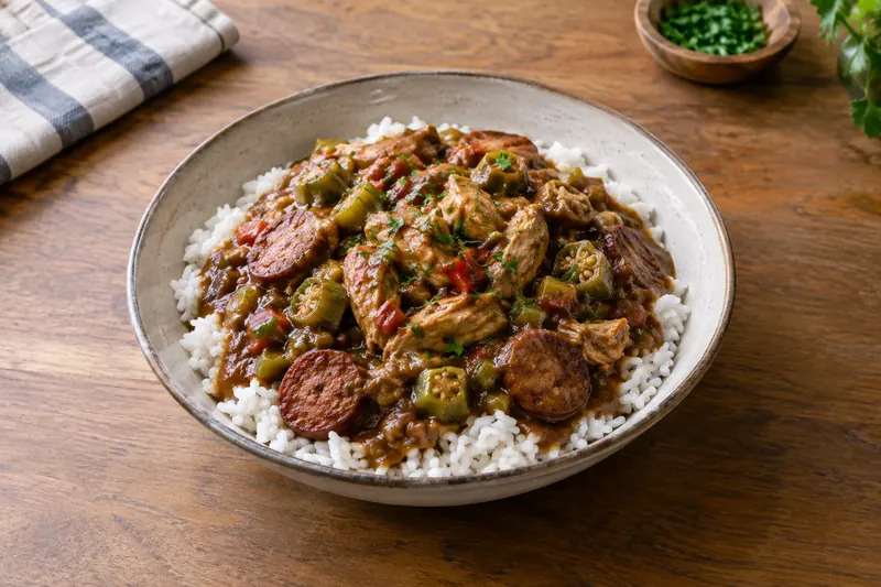 A bowl of dark brown gumbo with chicken, sausage and okra over white rice