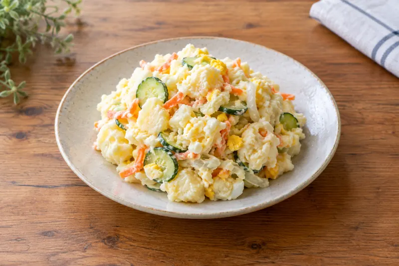 A scoop of creamy chunky potato salad with cucumber slices, carrot and egg