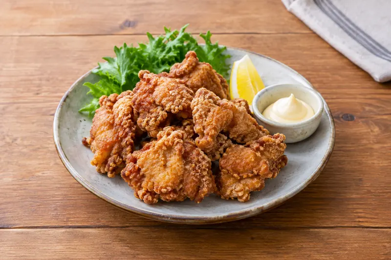 A pile of craggy golden fried chicken pieces with lemon wedges and Japanese mayonnaise