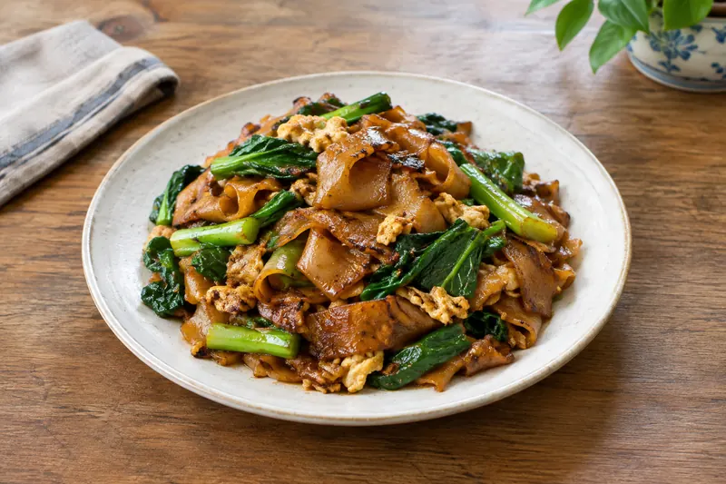 Wide charred rice noodles with Chinese broccoli, chicken and egg in a wok