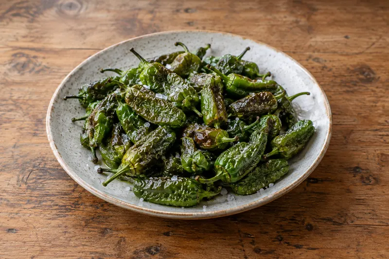Blistered green padrón peppers on a plate scattered with coarse sea salt