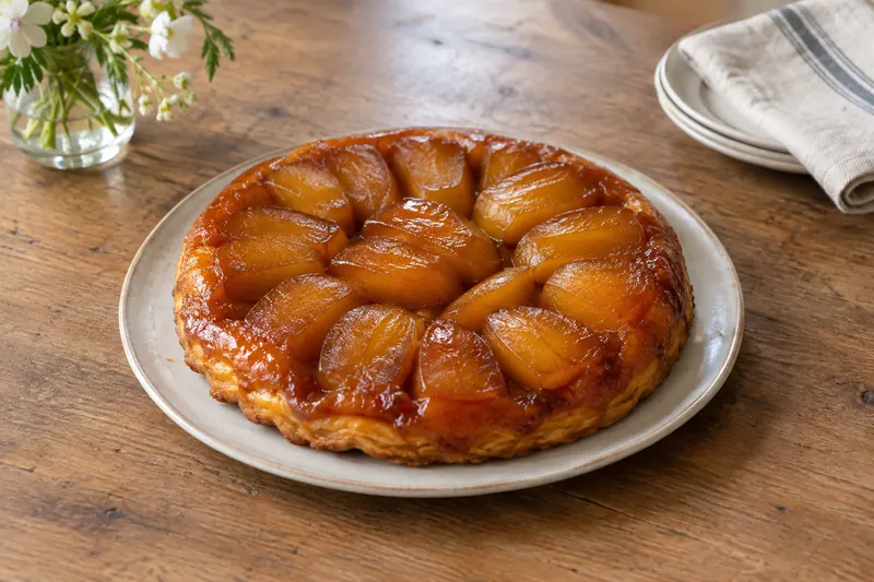 An inverted apple tart with glossy caramelised apple halves on top of golden pastry
